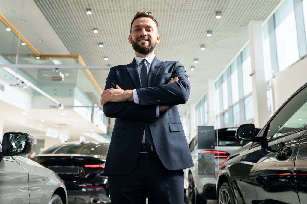 insurance company employee in a suit next to new cars in a car dealership